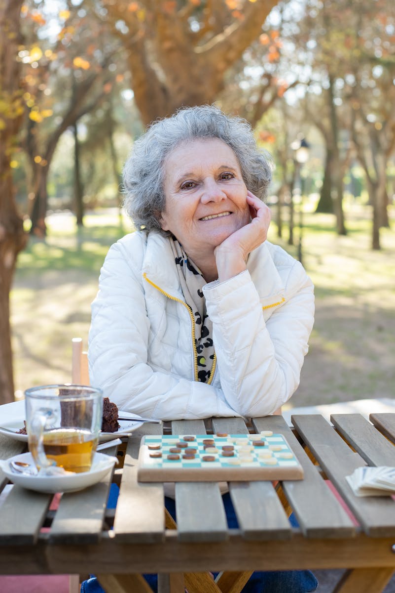 An elderly woman enjoys a relaxing board game outdoors in a sunny park setting.